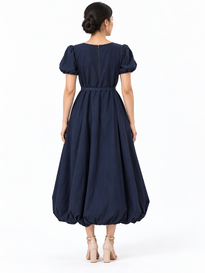 Back view of The Lamorah navy balloon-hem dress showing its center-back zipper, puff sleeves and narrow waist sash.