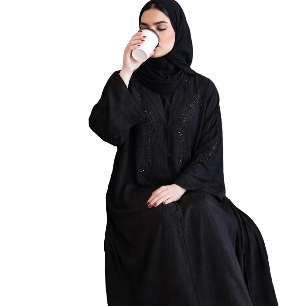 Black abaya with fine beaded sprays across the chest and sleeves, worn seated with a black shayla