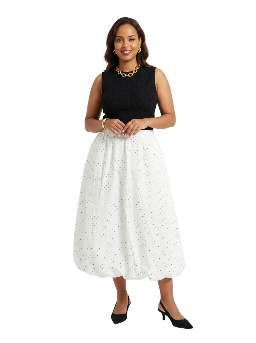 Front view of THE LAMORAH white polka-dot balloon midi skirt, styled with a black sleeveless top, gold necklace and black kitten heels.
