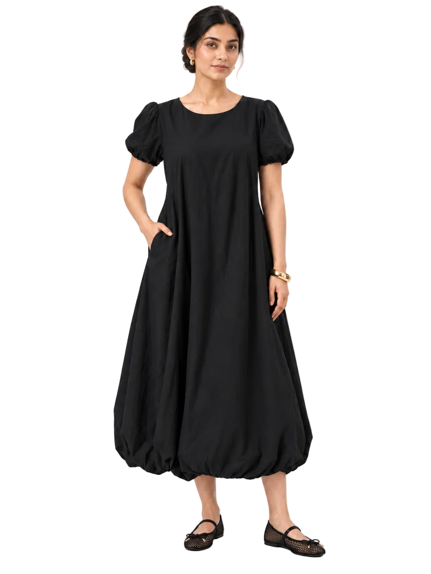 Full-length front view of The Lamorah black balloon-hem dress worn without its removable sash, with mesh Mary Jane flats and a gold cuff bracelet.