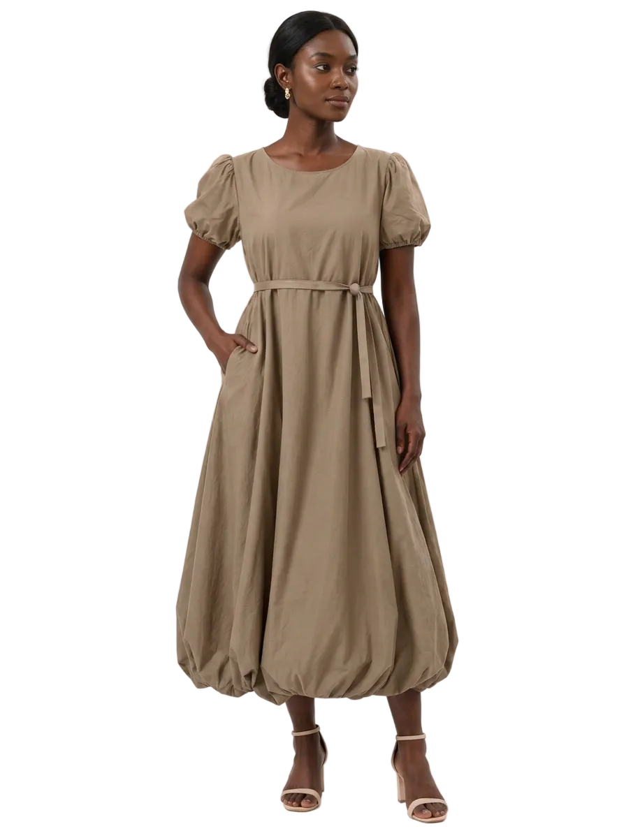 Model wearing The Lamorah taupe puff-sleeve balloon-hem dress with a narrow matching sash and one hand in a side pocket, front view.