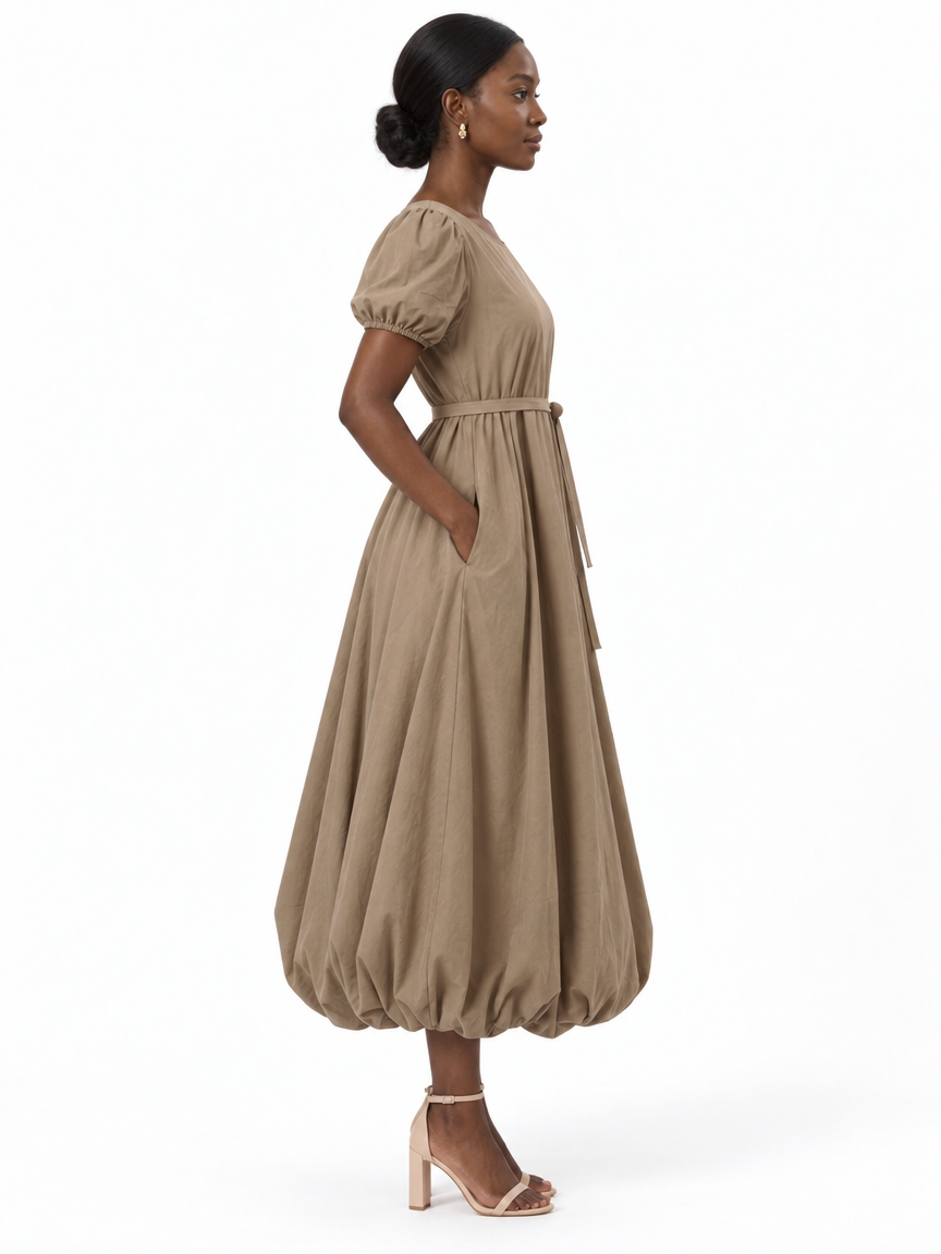 Side profile of The Lamorah taupe puff-sleeve dress showing its side pocket, separate waist sash and full rounded balloon hem.