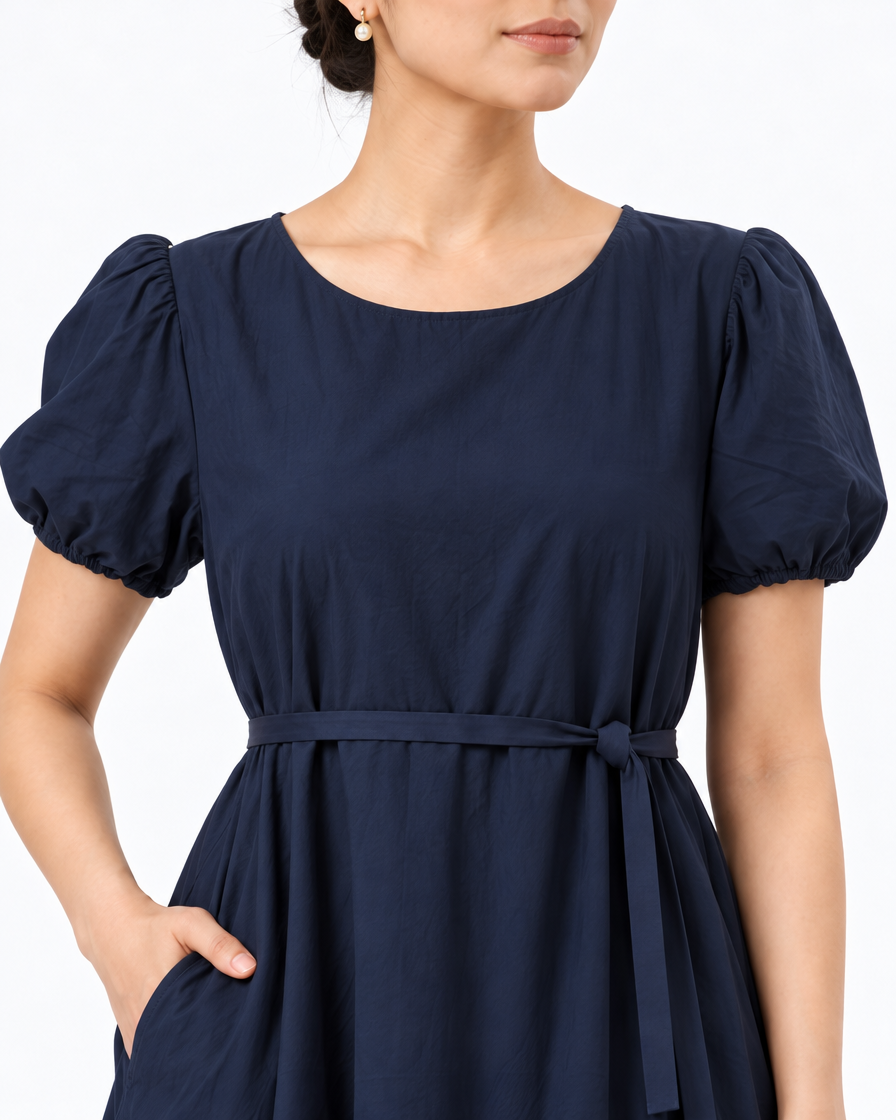 Close-up of The Lamorah navy dress showing the round neckline, short puff sleeves, pocket and separate narrow waist sash.