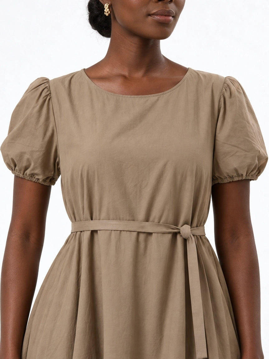 Close-up of The Lamorah taupe dress showing its round neckline, short puff sleeves, fabric texture and separate narrow matching sash.
