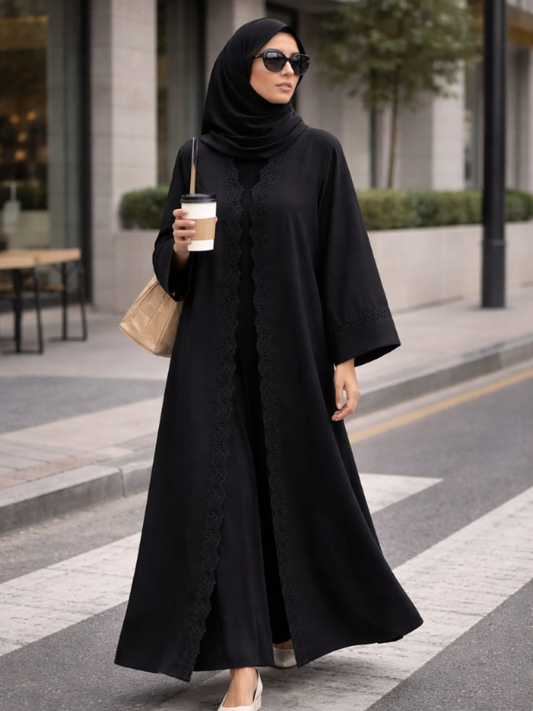 Woman in a black abaya holding a coffee cup on a city street. |THE LAMORAH
