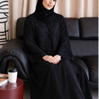Woman in a black abaya sitting on a black couch with a beige curtain in the background |THE LAMORAH

