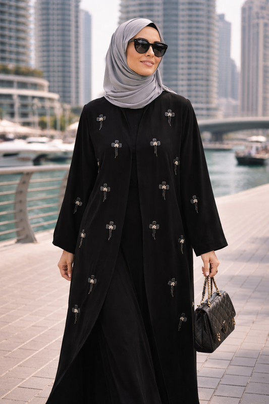 Woman in a black abaya with a gray hijab and sunglasses, holding a handbag, standing in an urban setting.|THE LAMORAH