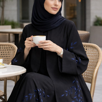 Woman in a black abaya with blue embroidery holding a cup outdoors.|THE LAMORAH
