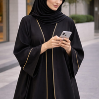 Woman in a black abaya with gold trim using a smartphone outdoors. |THE LAMORAH
