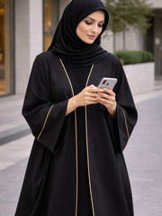 Woman in a black abaya with gold trim using a smartphone outdoors. |THE LAMORAH
