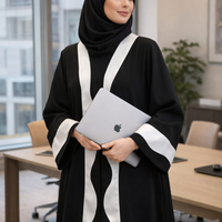 Woman in a black and white abaya holding an Apple laptop in an office setting.|THE LAMORAH
