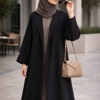 Woman in a black coat and hijab holding sunglasses, standing outdoors. |THE LAMORAH
