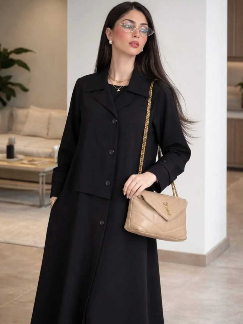 Woman in a black coat holding a beige handbag in an indoor setting |THE LAMORAH
