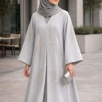 Woman in a light gray abaya with intricate designs standing outdoors.|THE LAMORAH
