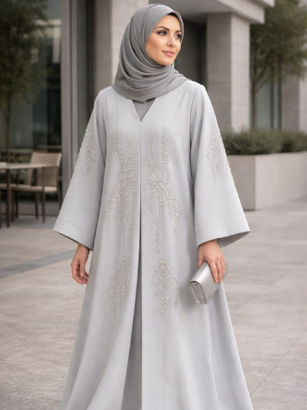 Woman in a light gray abaya with intricate designs standing outdoors.|THE LAMORAH
