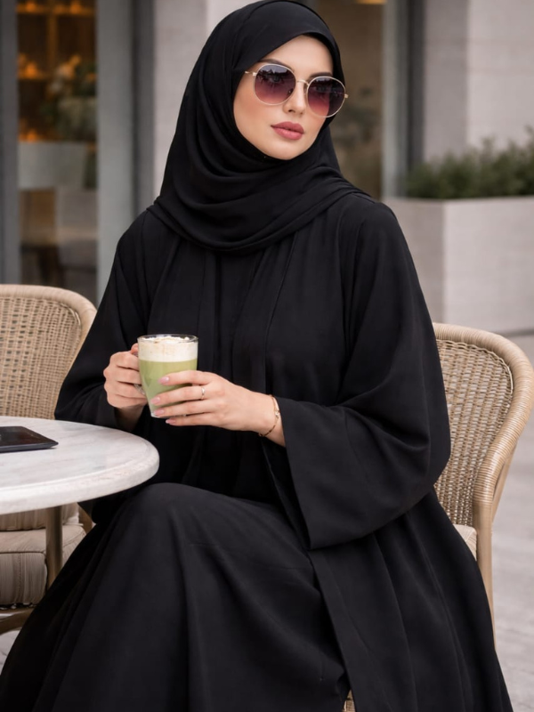 Woman in black abaya holding a drink outdoors |THE LAMORAH
