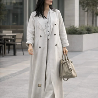 Woman wearing a long light gray coat and holding a handbag on a city street. |THE LAMORAH
