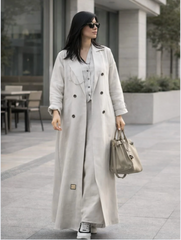 Woman wearing a long light gray coat and holding a handbag on a city street. |THE LAMORAH
