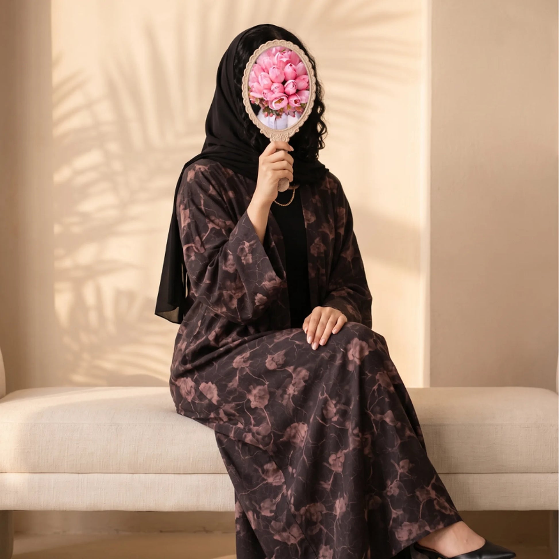 Plum abaya with a dusty rose watercolour floral print, worn seated with a black shayla