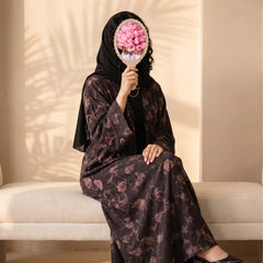 Plum abaya with a dusty rose watercolour floral print, worn seated with a black shayla