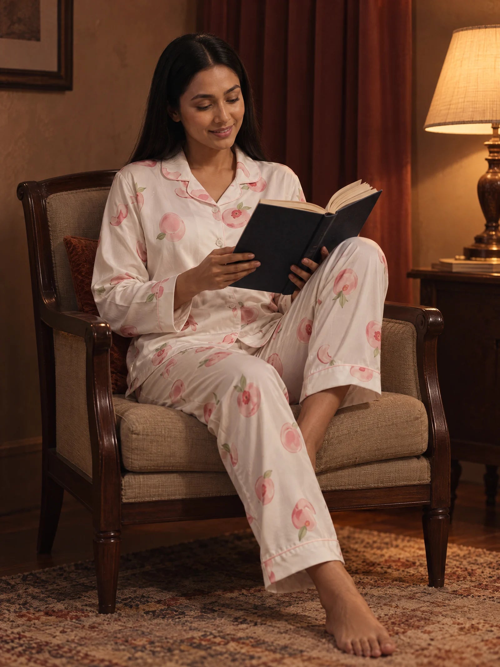 Woman relaxing in white peach-print pajamas and reading a book by warm evening lamplight